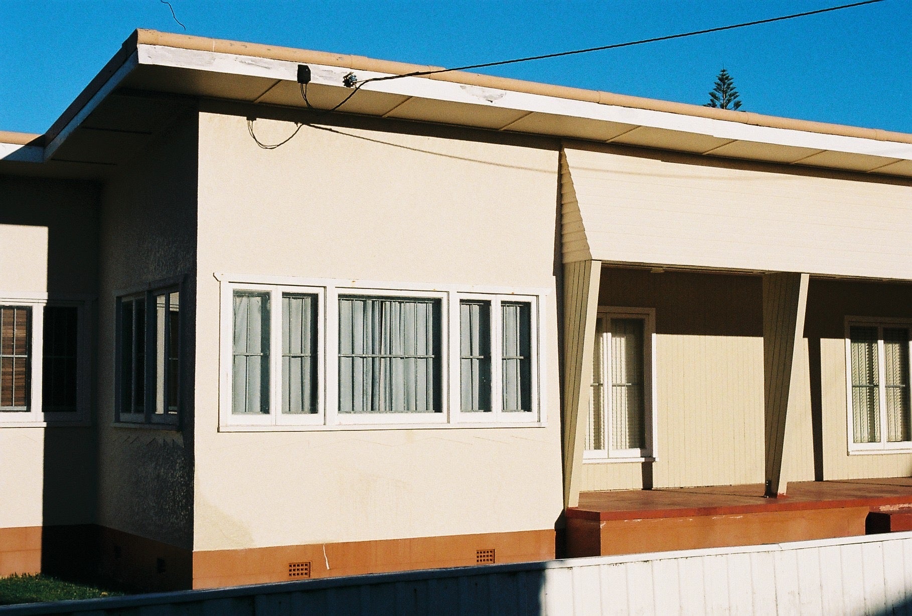 Beige house with a wooden deck and curtains on windows under a clear blue sky.